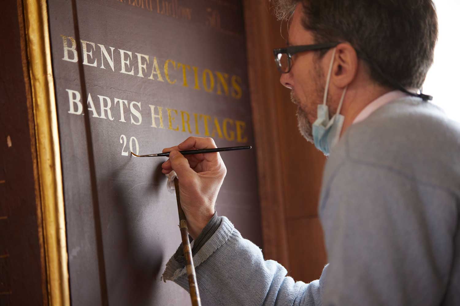 Signwriter adds names to a Benefactions panel in the Great Hall