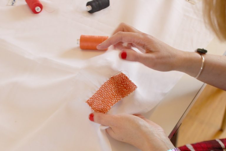 Orange thread being hand sewn onto white fabric.