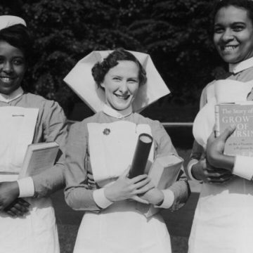 Three nurses stood in a row. One white nurse is flanked by two Black nurses. They hold prizes in their hands.