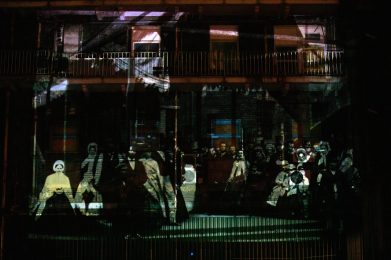 Projection onto outside of a building showing ghostly figures of men and women.