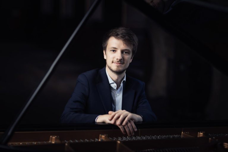 Man sat at a piano with his arms resting on the top.