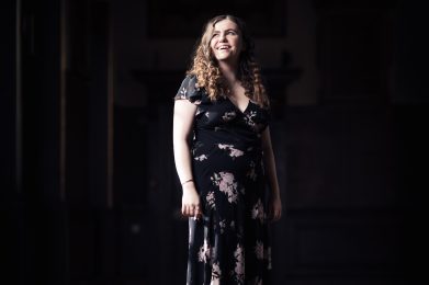 Woman standing in hall wearing a short sleeved floor length dress.