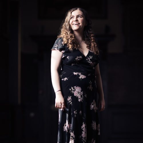 Woman standing in hall wearing a short sleeved floor length dress.