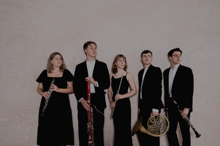 Standing group of three men and two women holding instruments.