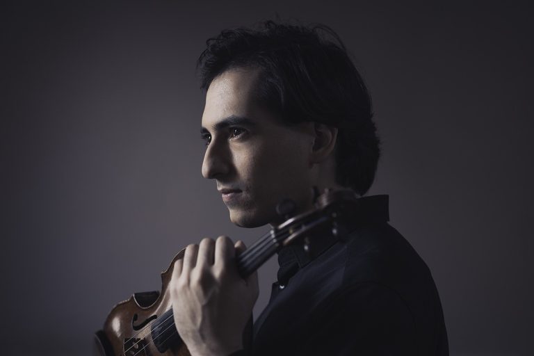 Man holding a violin close to this face.