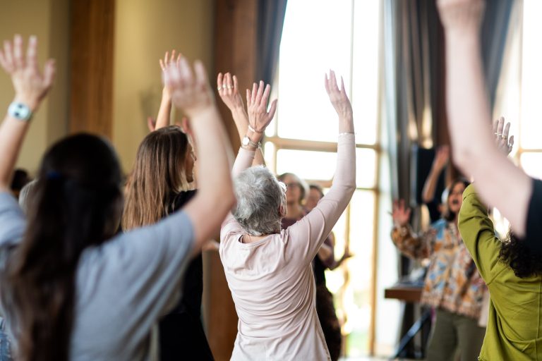 A group of women stood in a room with their arms raised above their heads.