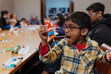 Boy holding a rocket made from LEGO in his right hand.