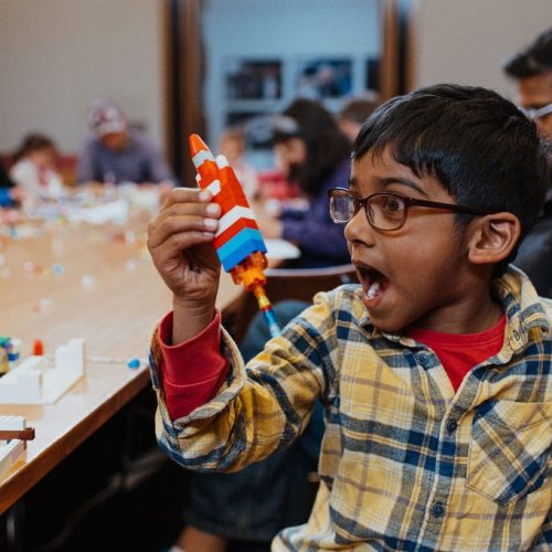 Boy holding a rocket made from LEGO in his right hand.