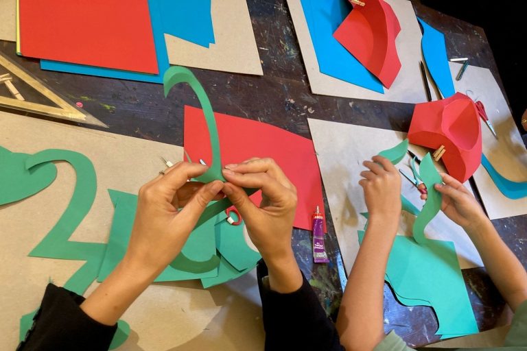 Image shows hand bending and folding coloured pieces of card. The table has card on it.