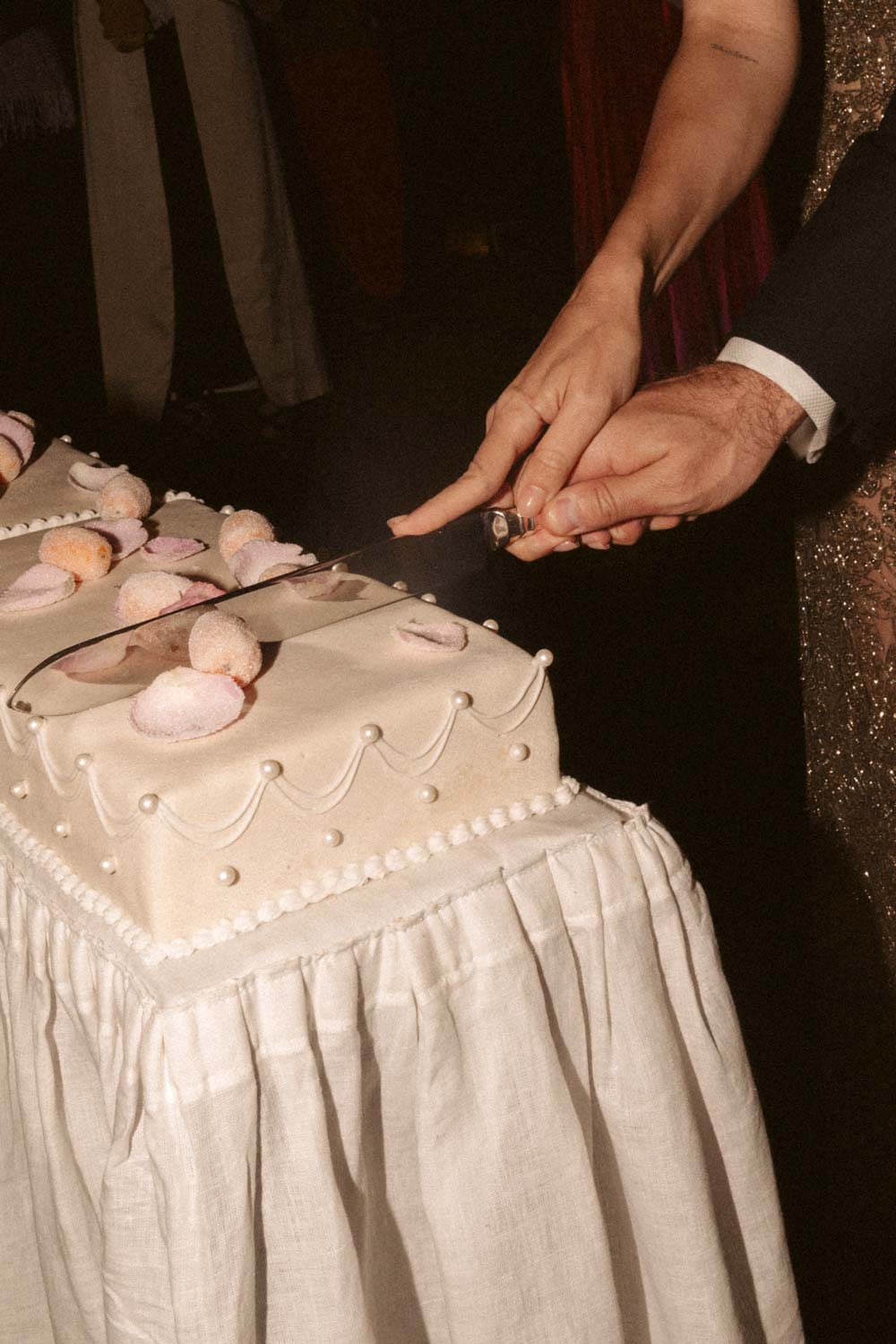 A bride and grooms hands join to cut a wedding cake
