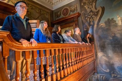 Six people stood against a stair banister looking at paintings.
