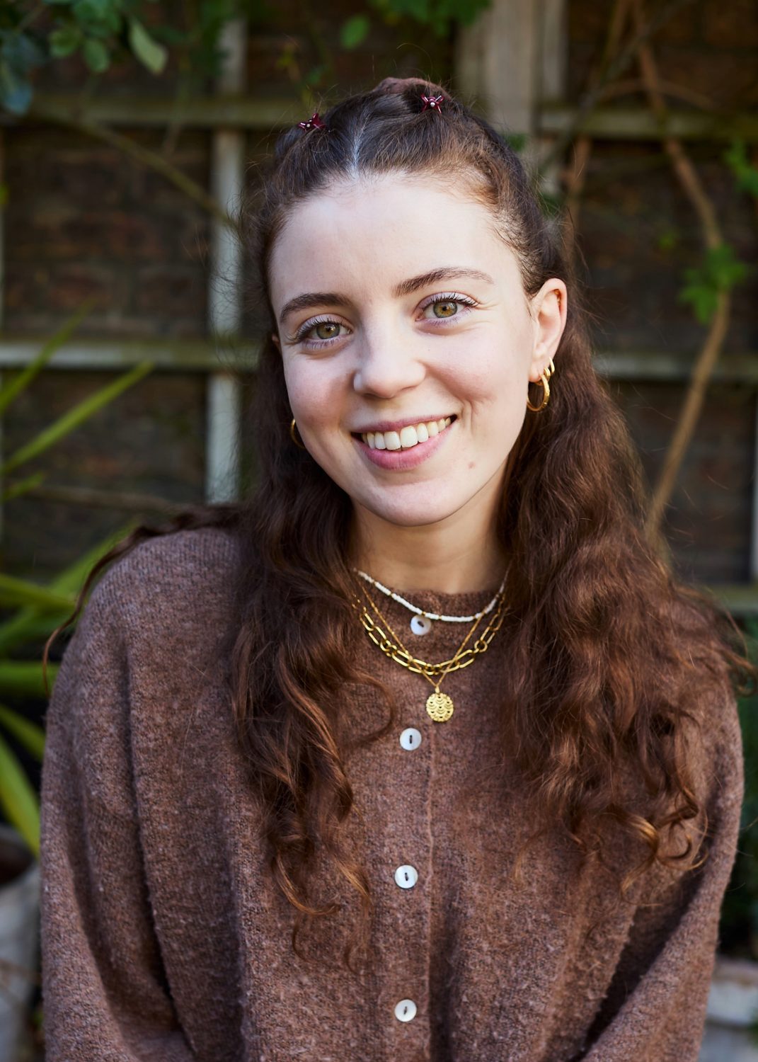 Close up image of woman smiling, she has gold earrings and wears the top section of her hair up in a bun.