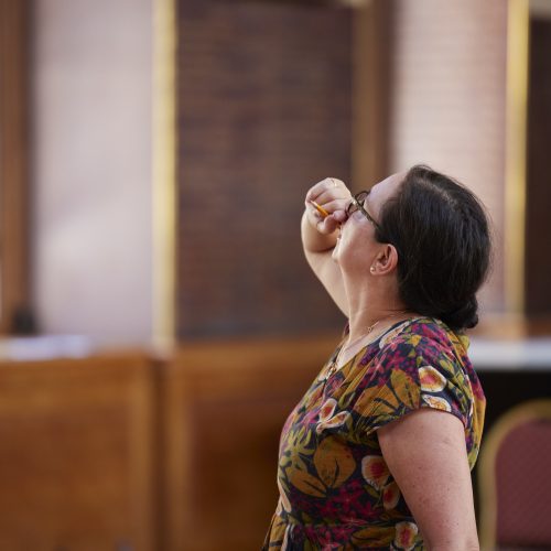 Woman stood looking upwards with her right hand to her face.